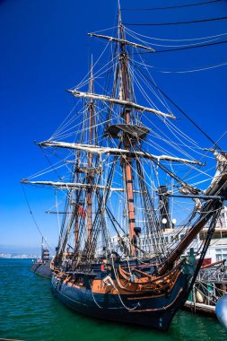 Uzun direkli ve yelkenli büyük bir gemi rıhtıma yanaştı. Gökyüzü berrak ve mavi, ve su sakin. Gemi tarihsel bir gemi gibi görünüyor ve görülmeye değer güzel bir manzara.