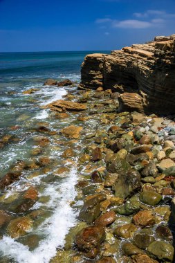 Okyanus sakin ve kayalar kıyı boyunca dağılmış. Kayalar çeşitli boyutlarda ve kıyı şeridi boyunca dağılmış. Su koyu mavi renktir ve gökyüzü açık ve mavidir