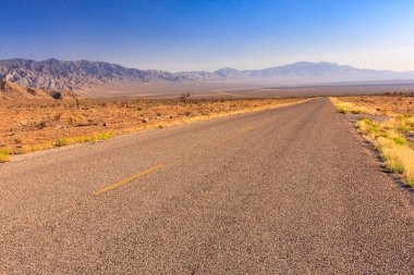 Arka planda dağlar olan çölde bir yol. Yol boş ve gökyüzü temiz.