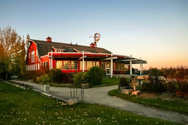 Beyaz çatılı ve saat kulesi olan kırmızı bir ahır. Ahır yemyeşil çimlerle çevrili.