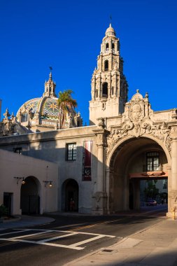 Tepesinde kubbe ve yüksek kulesi olan büyük bir bina. Bina yaya geçidi olan bir cadde ve yan tarafa park edilmiş birkaç araba ile çevrili.