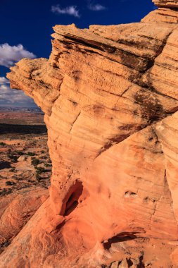 İçinde delik olan kayalık bir uçurum. Delik kırmızı bir kaya duvarla çevrilidir. Gökyüzü mavi ve güneş parlıyor.