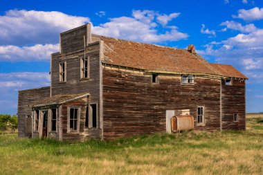 Kırmızı çatılı büyük, eski bir bina bir tarlada duruyor. Bina terk edilmiş ve bakımsız görünüyor.