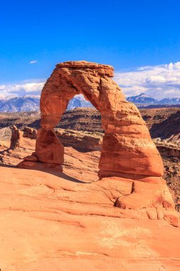Büyük bir kaya kemeri çölün ortasındadır. Kemer yolu dağlarla çevrili ve gökyüzü temiz. Sahne huzurlu ve sakin, kemer yolu görüntünün odak noktası.