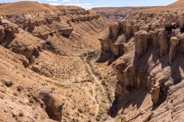 İçinden nehir akan bir çöl kanyonu. Kanyon kayalık ve çorak, görünürde bitki örtüsü yok. Gökyüzü açık ve güneş parlak, sıcak ve davetkar bir atmosfer yaratıyor.