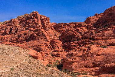 Arka planda mavi gökyüzü olan kayalık bir dağ sırası. Dağlar kırmızı ve gökyüzü berrak