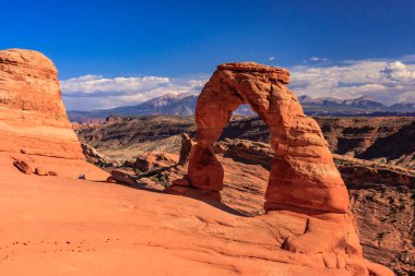 Ortasında büyük bir kemer olan bir kanyon. Gökyüzü mavi ve dağlar arka planda.
