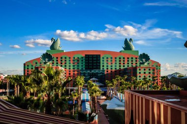 Arka planda bir sürü palmiye ağacı ve mavi gökyüzü olan büyük bir otel. Otel çok renkli ve çok fazla detaya sahip.