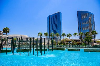 Ortasında çeşme olan büyük bir su kütlesi. Çeşme bir sürü yeşil palmiye ağaçlarıyla çevrilidir. Gökyüzü açık ve mavi