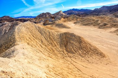Arkasında büyük bir tepe olan bir çöl manzarası. Tepe toprak ve kayalarla kaplı.