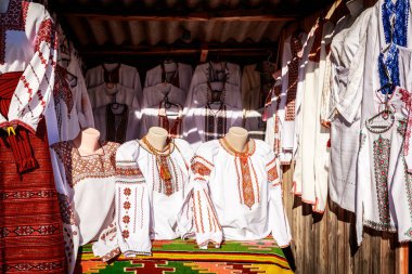 Kırmızı aksanlı beyaz giysi gösterisi. Giysiler askıda asılı. Görüntü yabancı bir dilde.