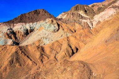 Kayalık, kahverengi ve yeşil yamaçlı bir dağ sırası. Tepenin renkleri kahverengi, yeşil ve mavinin karışımıdır.