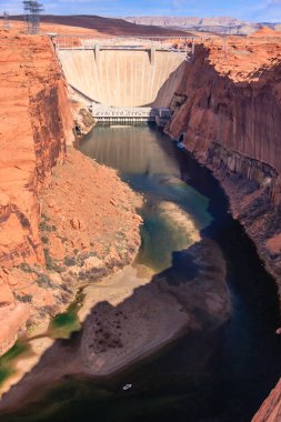 Arka planda baraj olan bir nehir. Su yeşil ve kayalar kırmızı.