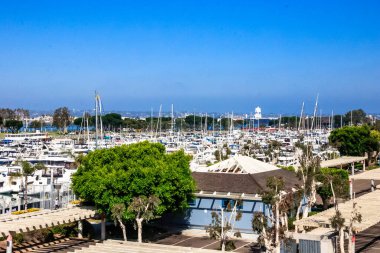 Bir marinaya büyük bir grup tekne yanaştı. Gökyüzü açık ve mavi, ve ağaçlar yeşil