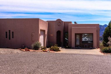 Beyaz garaj kapısı olan büyük bir ev çakıllı bir garaj yolunda duruyor. Ev birkaç saksı bitkisi olan küçük bir bahçeyle çevrili.