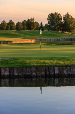Yeşil üzerinde bayrak olan bir golf sahası. Bayrak beyaz ve tee noktasında