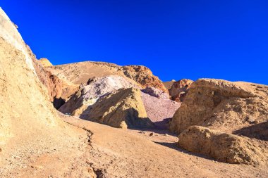 Arka planda mavi gökyüzü olan bir dağ sırası. Dağlar, kayalar ve toprakla kaplı.