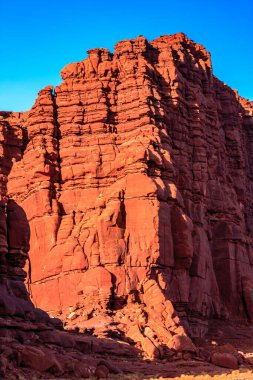 Arka planda mavi gökyüzü olan büyük bir kaya oluşumu. Kayalar kırmızı ve gökyüzü berrak
