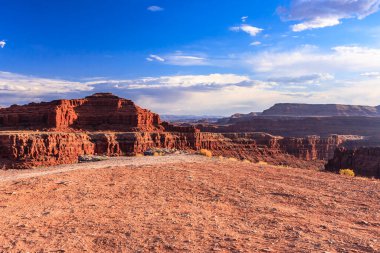 Arkasında dağ olan bir çöl manzarası. Gökyüzü mavi ve güneş parlıyor.