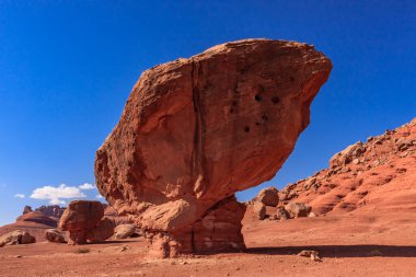 Üzerinde açık mavi bir gökyüzü olan büyük bir kaya oluşumu çölde bulunur. Kaya manzarada belirgin bir özelliktir ve doğal bir mucize gibi görünüyor. Huzurlu ve huzurlu bir sahne.