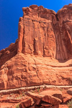Arka planda mavi gökyüzü olan büyük bir kaya oluşumu. Kaya oluşumu kırmızı ve kahverengi kayalardan oluşur.