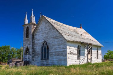 Çan kulesi ve üzerinde haç olan küçük, eski bir kilise. Bina beyaz ve bir sürü penceresi var. Gökyüzü mavi ve berrak