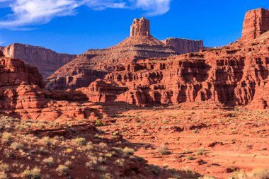 Arkasında dağ olan bir çöl manzarası. Gökyüzü mavi ve güneş parlıyor.