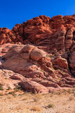 Arka planda mavi gökyüzü olan kayalık bir dağ. Dağ kırmızı ve kahverengidir.