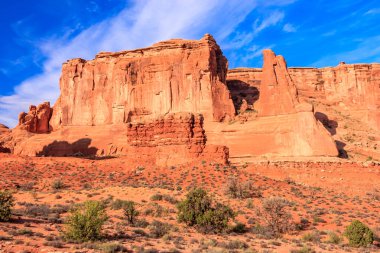 Açık mavi gökyüzü olan kayalık bir dağ sırası. Gökyüzü bulutlarla kaplı ve güneş ışıl ışıl parlıyor. Manzara kuru ve çorak.