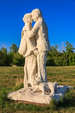 Bir çift bir heykelde tasvir edilir, bir kişi diğerini tutarken. Heykel beyazdır ve çimenlik bir alana yerleştirilmiştir. Sahne huzurlu ve romantiktir. Çiftin birbirini kucakladığını görüyoruz.