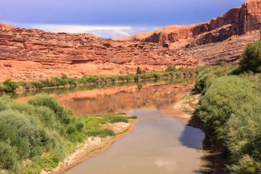 Bir nehir kayalık bir kıyı şeridi olan bir kanyondan akar. Su kahverengi ve bulanıktır ve çevresindeki bitki örtüsü seyrektir. Sahne huzurlu ve huzurlu.