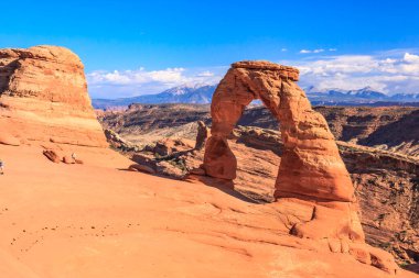 Ortasında büyük bir kemer olan bir kanyon. Kemer yolu bir çöl manzarasıyla çevrilidir.