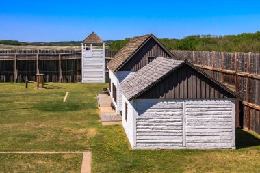 Siyah çatılı küçük beyaz bir bina çimenli bir arazide duruyor. Bina ahşap bir çitle çevrili.