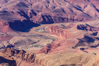 Bir nehir kırmızı kayalarla dolu bir kanyondan geçiyor. Kanyon dağlarla çevrili ve nehir kahverengi.