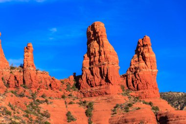 Üç uzun kırmızı kaya oluşumuna sahip kayalık bir dağ sırası. Gökyüzü açık ve mavidir, ve güneş parlıyor. Manzaranın doğal güzelliğine hayranlık ve hayret kavramı