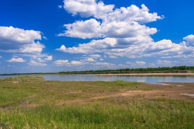Güzel mavi bir gökyüzü, birkaç bulut ve büyük bir su kütlesi. Gökyüzü açık ve su sakin.