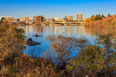 Nehir ve köprüsü olan güzel bir şehir manzarası. Su sakin ve ağaçlar sonbahar renginde.