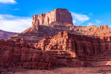 Tepesinde büyük bir kaya olan bir dağ. Gökyüzü mavi ve güneş parlıyor. Dağ kayalık bir manzarayla çevrilidir.