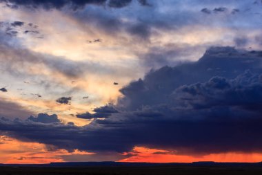 Gökyüzü bulutlarla dolu ve güneş batıyor. Bulutlar karanlık ve gökyüzü turuncu ve mavi karışımı.
