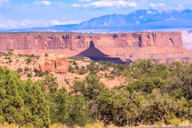 Aralarında vadi olan bir dağ sırası. Vadi ağaçlar ve kayalarla çevrilidir. Gökyüzü mavi ve güneş parlıyor.