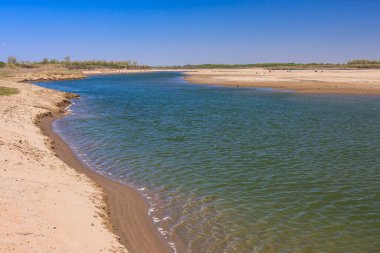 Bir su kütlesi kumlu bir plajla çevrilidir. Su sakin ve berrak. Kumsal da boş.