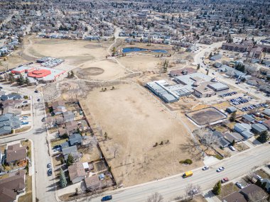 Büyük boş bir arazisi olan bir yerleşim yeri manzarası. Evler dağılmış ve caddeye park etmiş birkaç araba var.
