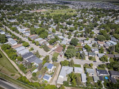 Evleri ve ağaçları olan bir yerleşim yeri. Evlerin çoğu beyaz ve ağaçlar yeşil. Sokaklar evlerle dolu ve caddeye park edilmiş arabalar var.