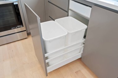 Gümüş fırını ve beyaz çöp tenekesi olan bir mutfak. Çöp kutusu diğer iki çöp tenekesiyle birlikte çekmecede.