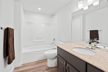 Banyoda beyaz bir tuvalet ve duvarında kahverengi bir havlu asılı. Banyo temiz ve iyi aydınlatılmış.