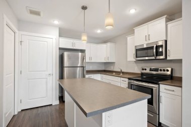 Beyaz buzdolabı, mikrodalga fırın ve sobası olan bir mutfak. Tezgah granitten yapılmış ve dolaplar beyaz.