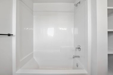 Beyaz küveti ve beyaz duşu olan beyaz bir banyo. Duş boş ve küvet de boş.