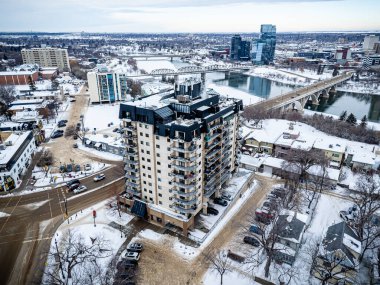 Merkezinde büyük bir bina bulunan karlı bir şehir manzarası. Gökyüzü bulutlu ve kar yağıyor