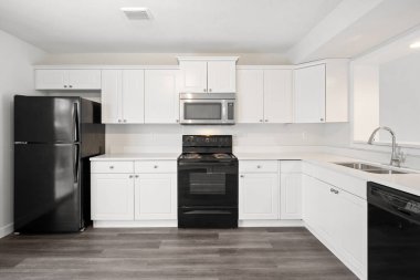 Siyah ocağı ve beyaz buzdolabı olan bir mutfak. Mutfak boş ve temiz.