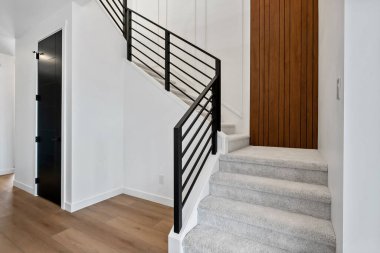 Siyah parmaklıklı ve ahşap kapılı bir merdiven. Merdiven beyaz halıdan yapılmıştır. Kapı kahverengi ve siyah saplı.